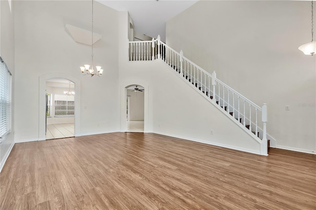 unfurnished living room featuring hardwood / wood-style flooring, ceiling fan with notable chandelier, and a towering ceiling