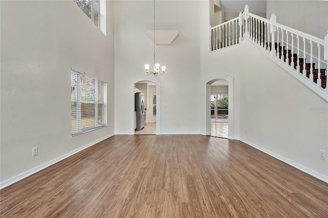 unfurnished living room with a notable chandelier, light hardwood / wood-style floors, and a towering ceiling