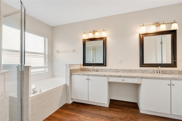 bathroom with hardwood / wood-style floors, vanity, and a relaxing tiled tub