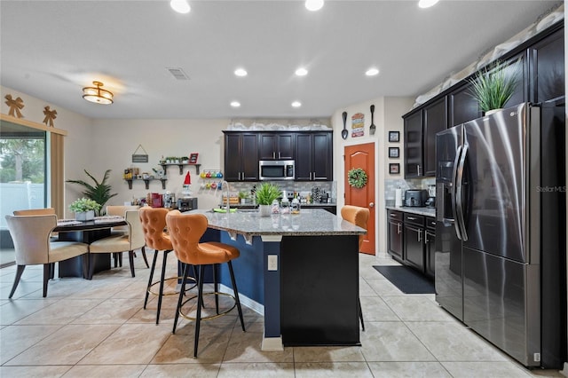 kitchen featuring tasteful backsplash, light stone counters, stainless steel appliances, light tile patterned floors, and a center island