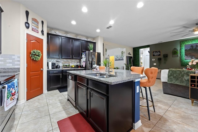 kitchen featuring a kitchen bar, appliances with stainless steel finishes, a center island with sink, and decorative backsplash