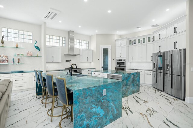 kitchen featuring wall chimney range hood, sink, appliances with stainless steel finishes, a kitchen bar, and a large island with sink