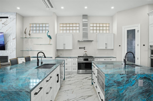 kitchen with a large island, sink, wall chimney range hood, and appliances with stainless steel finishes