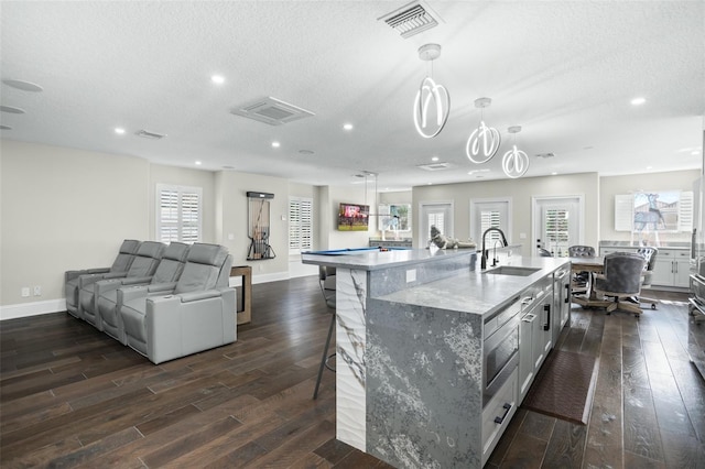 kitchen with sink, decorative light fixtures, a center island with sink, dark hardwood / wood-style floors, and a kitchen breakfast bar