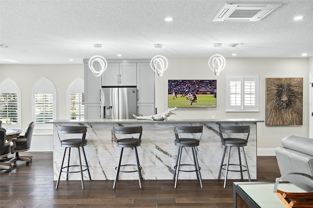 kitchen with stainless steel refrigerator with ice dispenser, a breakfast bar, plenty of natural light, dark hardwood / wood-style flooring, and pendant lighting