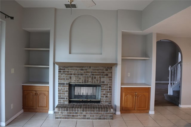 unfurnished living room featuring ceiling fan, built in features, light tile patterned floors, and a brick fireplace