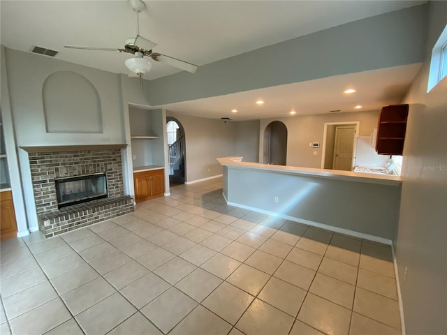 unfurnished living room featuring a fireplace, light tile patterned floors, built in features, and ceiling fan