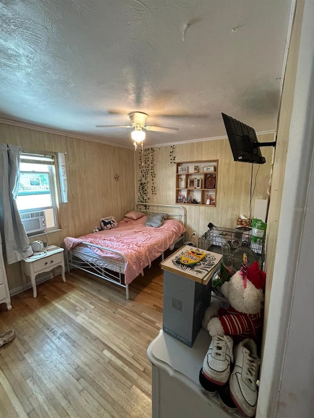 bedroom with wood walls, crown molding, ceiling fan, light wood-type flooring, and a textured ceiling