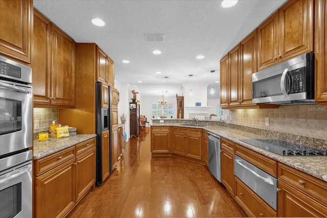 kitchen featuring sink, light hardwood / wood-style flooring, kitchen peninsula, pendant lighting, and appliances with stainless steel finishes