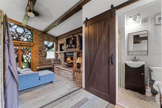 interior space with vanity, a stone fireplace, hardwood / wood-style flooring, ceiling fan, and toilet