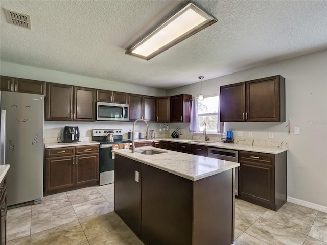 kitchen with appliances with stainless steel finishes, a kitchen island with sink, pendant lighting, and sink