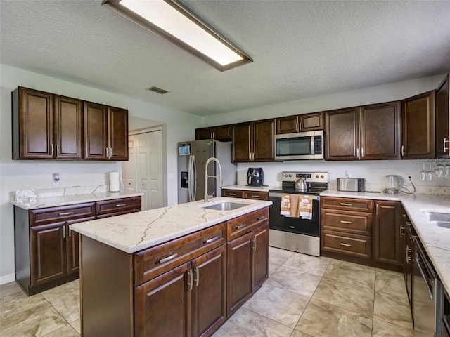 kitchen featuring a textured ceiling, sink, stainless steel appliances, and an island with sink