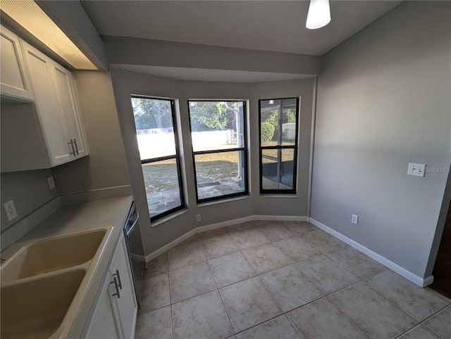 kitchen with dishwasher, light tile patterned flooring, white cabinetry, and sink