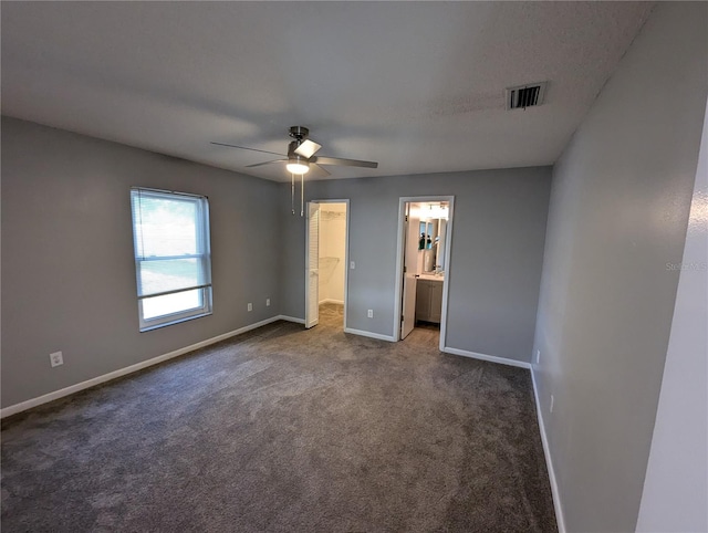 unfurnished bedroom featuring ensuite bath, ceiling fan, and dark carpet