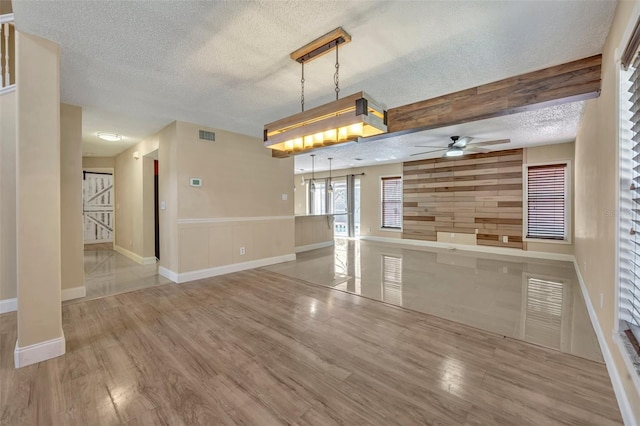 interior space with a textured ceiling, ceiling fan, light hardwood / wood-style flooring, and wood walls