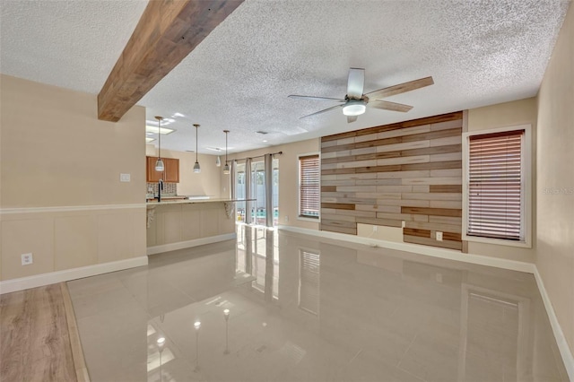 interior space with ceiling fan, beam ceiling, a textured ceiling, and wooden walls