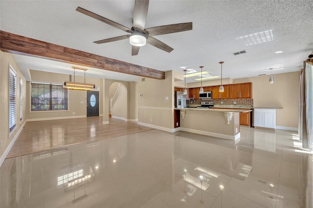 unfurnished living room with a textured ceiling, ceiling fan, sink, light tile patterned floors, and beamed ceiling