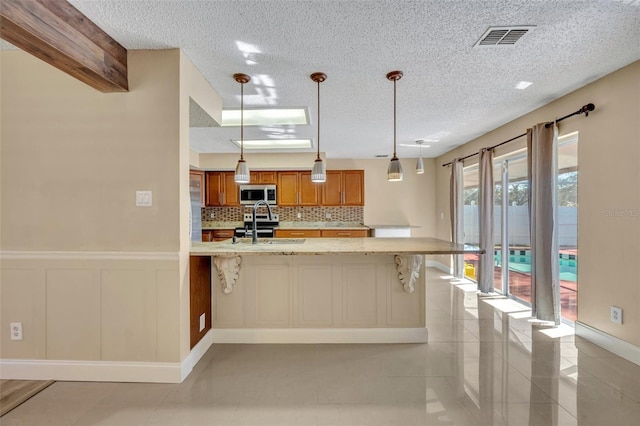 kitchen with light stone countertops, hanging light fixtures, stainless steel appliances, backsplash, and a kitchen bar