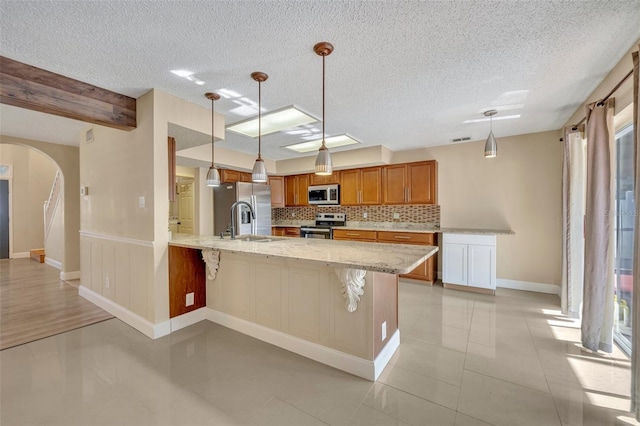 kitchen featuring kitchen peninsula, appliances with stainless steel finishes, backsplash, hanging light fixtures, and a breakfast bar area