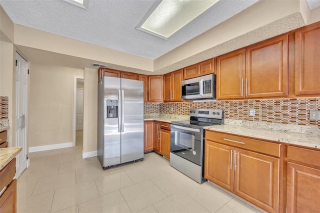 kitchen with tasteful backsplash, light stone counters, a textured ceiling, stainless steel appliances, and light tile patterned floors