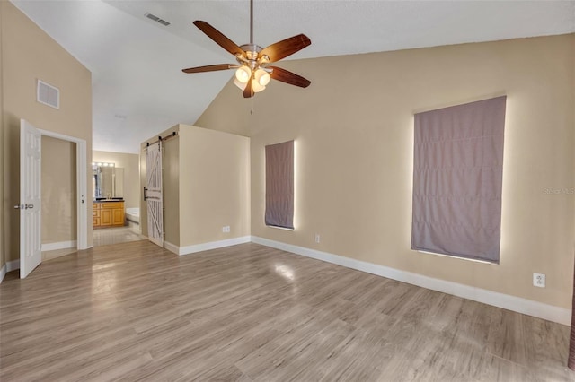 interior space featuring a barn door, ceiling fan, lofted ceiling, and light wood-type flooring