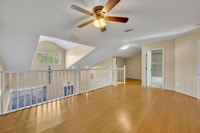 additional living space with a textured ceiling, ceiling fan, light hardwood / wood-style flooring, and lofted ceiling