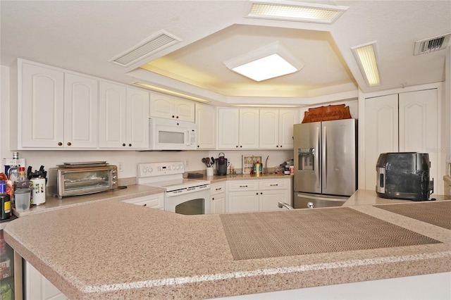 kitchen featuring kitchen peninsula, white appliances, a tray ceiling, and white cabinetry