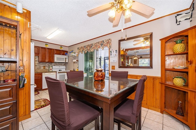 dining area featuring light tile patterned floors, ornamental molding, a textured ceiling, and wooden walls