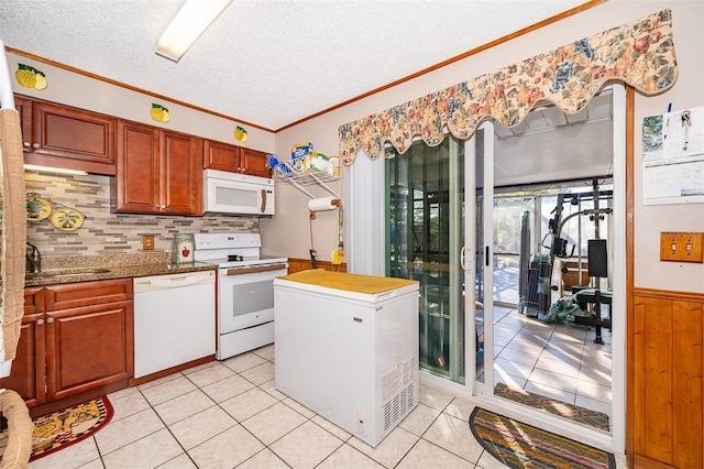 kitchen with wood walls, white appliances, sink, light tile patterned floors, and a textured ceiling