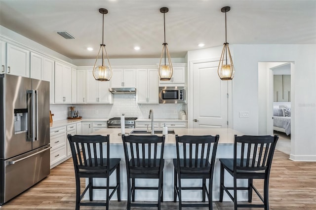 kitchen with white cabinets, decorative light fixtures, stainless steel appliances, and a center island with sink