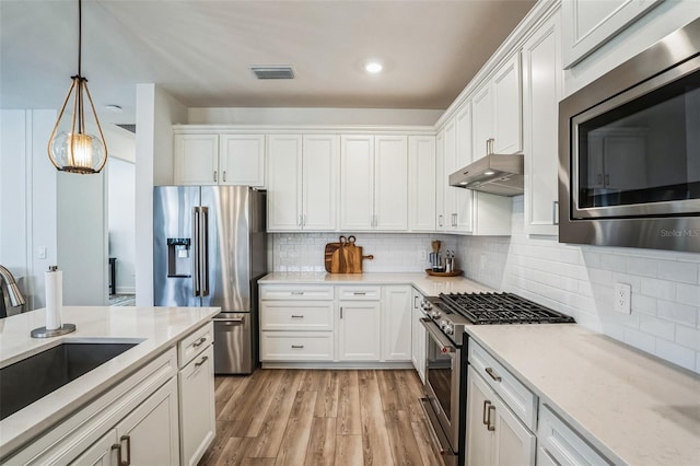 kitchen with high quality appliances, pendant lighting, white cabinets, and light stone counters