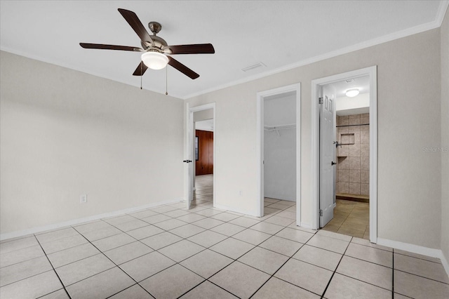 unfurnished bedroom with ceiling fan, a spacious closet, a closet, light tile patterned floors, and ornamental molding