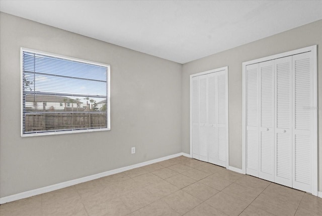 unfurnished bedroom with two closets and light tile patterned flooring