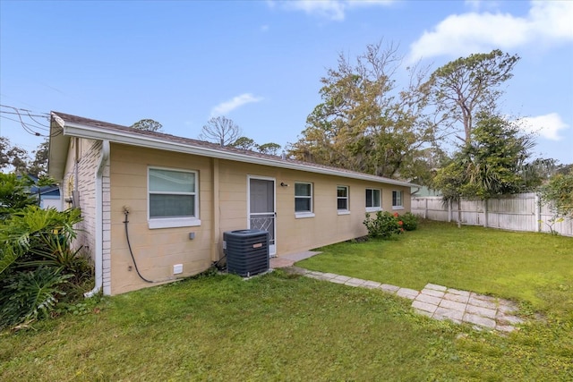 rear view of property featuring central air condition unit and a lawn