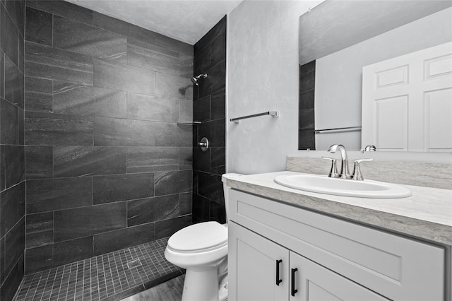 bathroom featuring a tile shower, vanity, and toilet