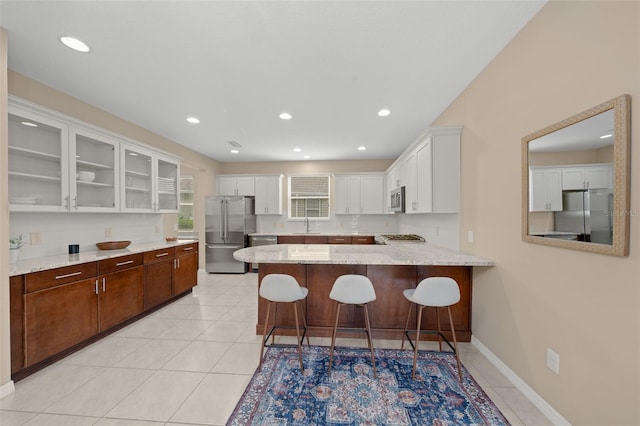 kitchen with kitchen peninsula, appliances with stainless steel finishes, white cabinets, a breakfast bar area, and light tile patterned flooring