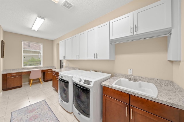 clothes washing area featuring cabinets, a textured ceiling, sink, washing machine and dryer, and light tile patterned flooring