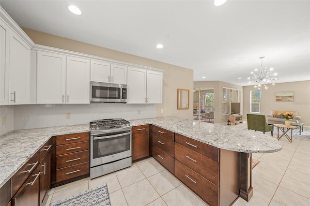 kitchen with kitchen peninsula, appliances with stainless steel finishes, white cabinets, a chandelier, and hanging light fixtures