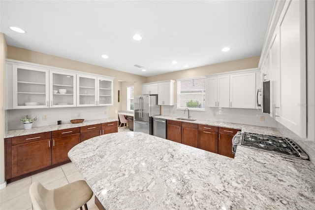 kitchen with a kitchen breakfast bar, stainless steel appliances, sink, light tile patterned floors, and white cabinetry