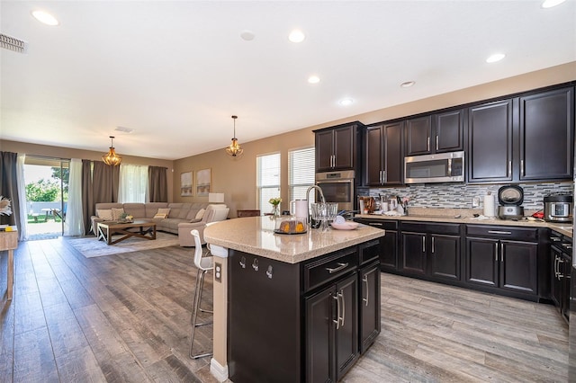 kitchen featuring pendant lighting, a center island with sink, a kitchen breakfast bar, decorative backsplash, and light wood-type flooring