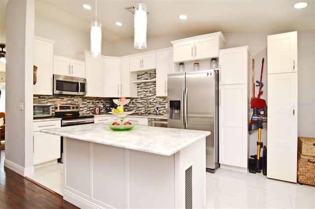 kitchen featuring white cabinets, decorative light fixtures, stainless steel appliances, and a kitchen island