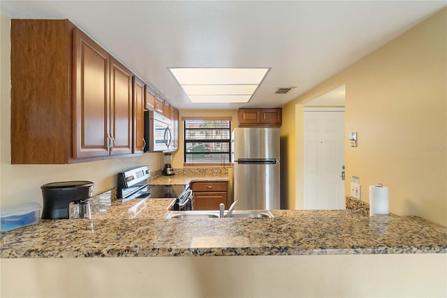 kitchen with kitchen peninsula, appliances with stainless steel finishes, light stone counters, and sink