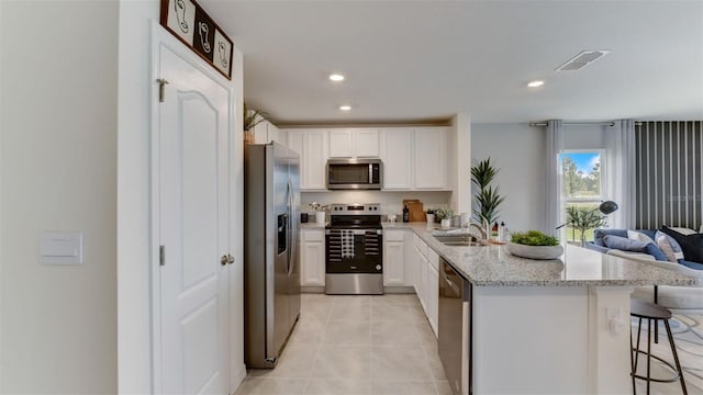 kitchen with light stone countertops, appliances with stainless steel finishes, white cabinetry, a breakfast bar area, and light tile patterned flooring