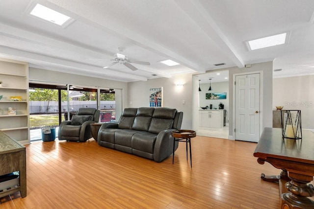 living area with a skylight, visible vents, light wood-style flooring, ceiling fan, and beamed ceiling