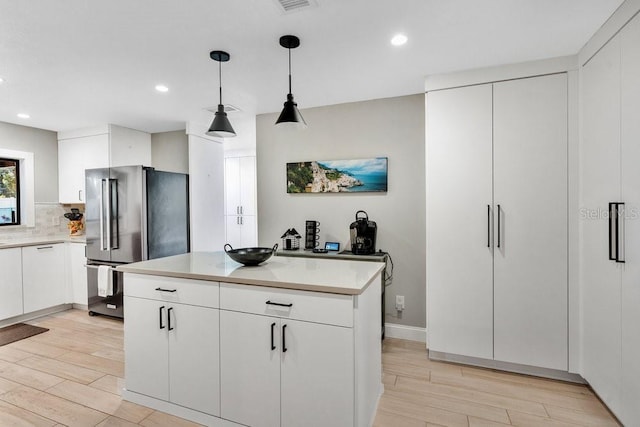 kitchen with light wood-style flooring, freestanding refrigerator, light countertops, and backsplash