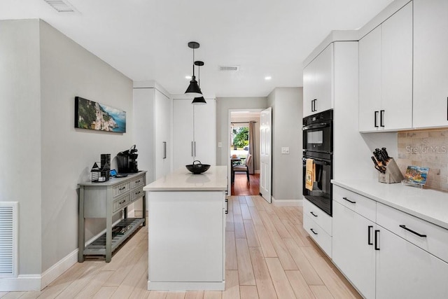 kitchen with a center island, visible vents, light wood-style flooring, backsplash, and white cabinetry