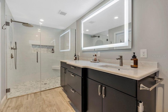 bathroom featuring double vanity, a stall shower, visible vents, wood finished floors, and a sink