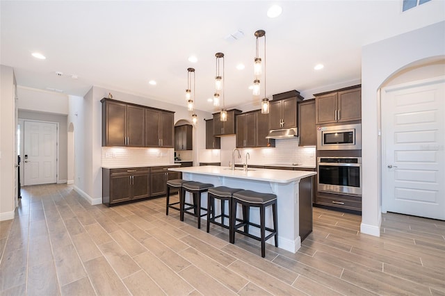 kitchen with pendant lighting, sink, a kitchen island with sink, appliances with stainless steel finishes, and dark brown cabinets