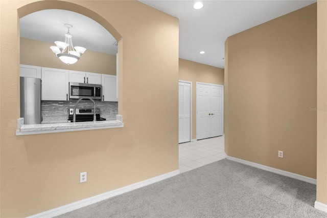 kitchen with a chandelier, light colored carpet, decorative backsplash, white cabinets, and appliances with stainless steel finishes