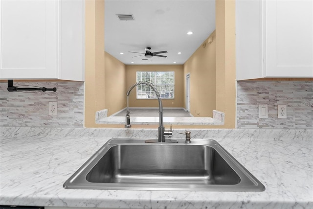 kitchen with tasteful backsplash, white cabinetry, sink, and ceiling fan